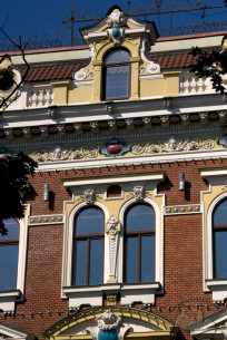Просп. Свободи, 27. Вікна IV-го  пов. з обрамленнями і лінійними сандриками; вінцевий карниз фасаду із ліпним фризом з маскаронами, рослинним орнаментом та картушами; аттик